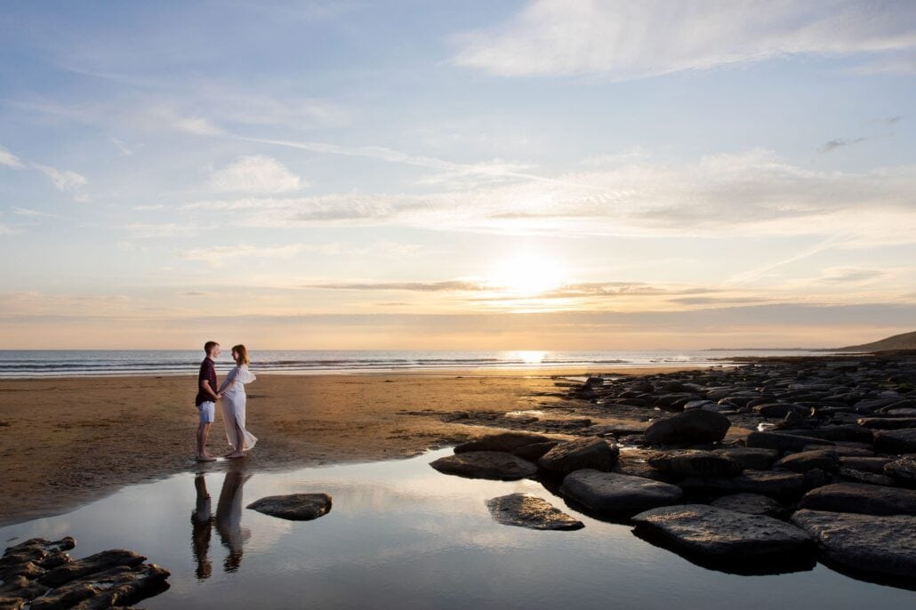 A couple standing on a beach at sunset.