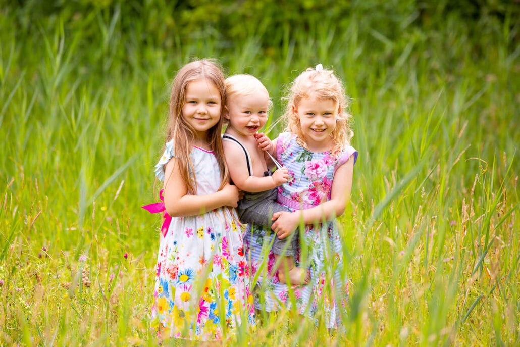 Three children standing in a field of tall grass.