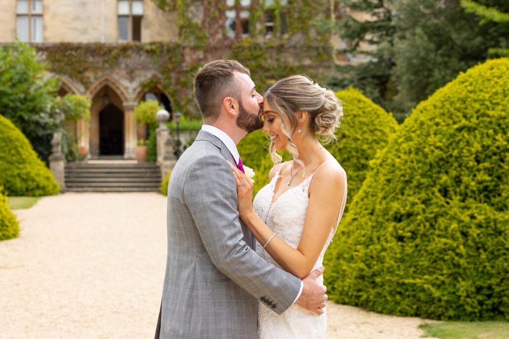 A south wales wedding photographer captures an embracing bride and groom in front of a manor house.