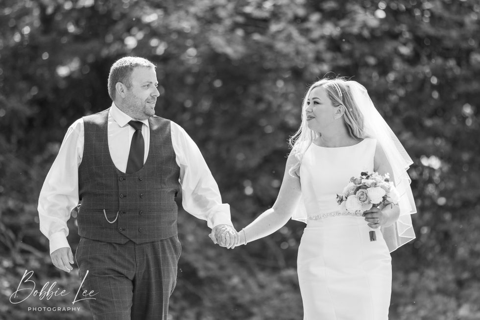 Black and white photo of a bride and groom holding hands.