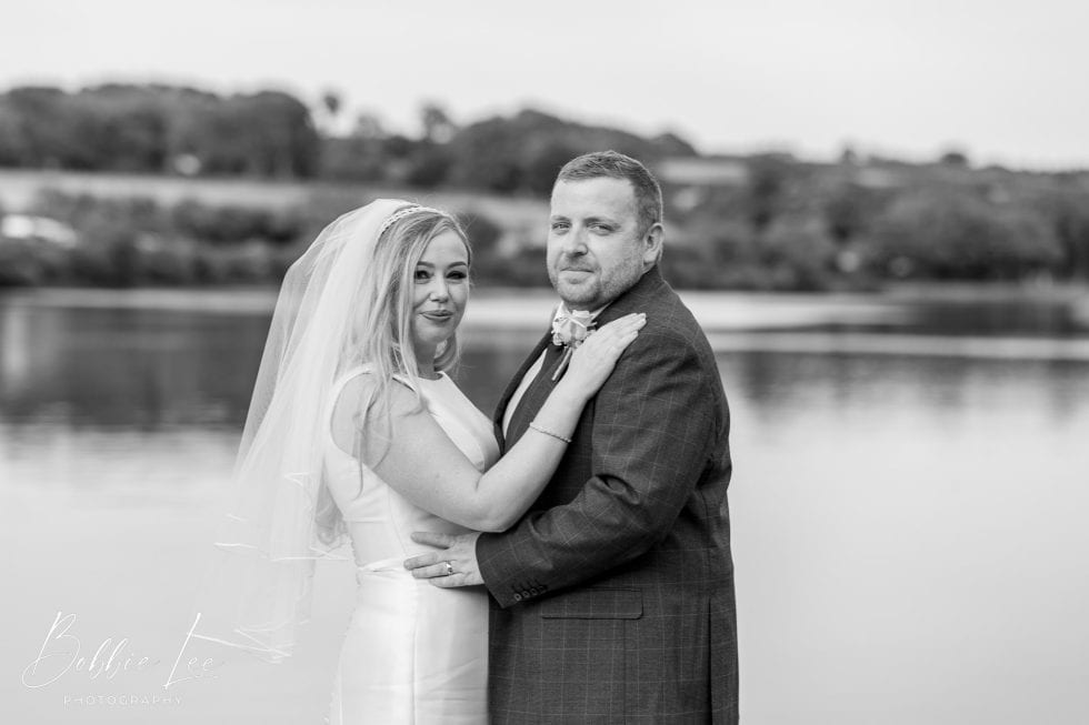 A bride and groom standing next to a lake in black and white.