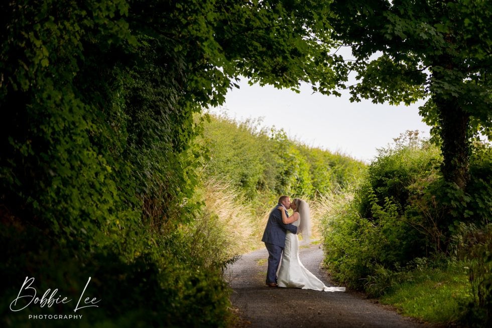 A bride and groom kissing on a country road.