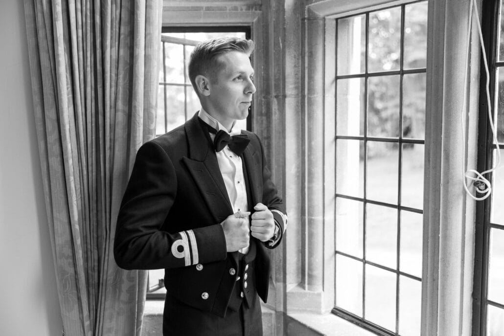 A South Wales wedding photographer capturing a man in a tuxedo standing by a window.