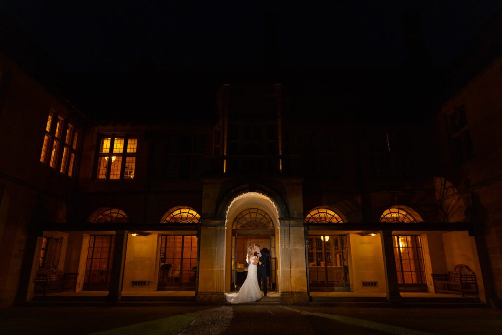 A stunning South Wales wedding photograph capturing a bride and groom, elegantly posed in front of a grand mansion under the enchanting night sky.