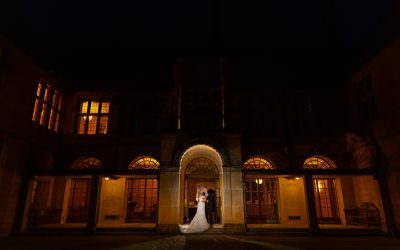 A bride and groom standing in front of a mansion at night.