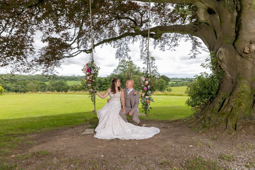 A south Wales wedding photographer capturing a couple sitting on a swing under a tree.