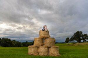 A south wales wedding photographer capturing a bride and groom sitting on hay bales in a field.