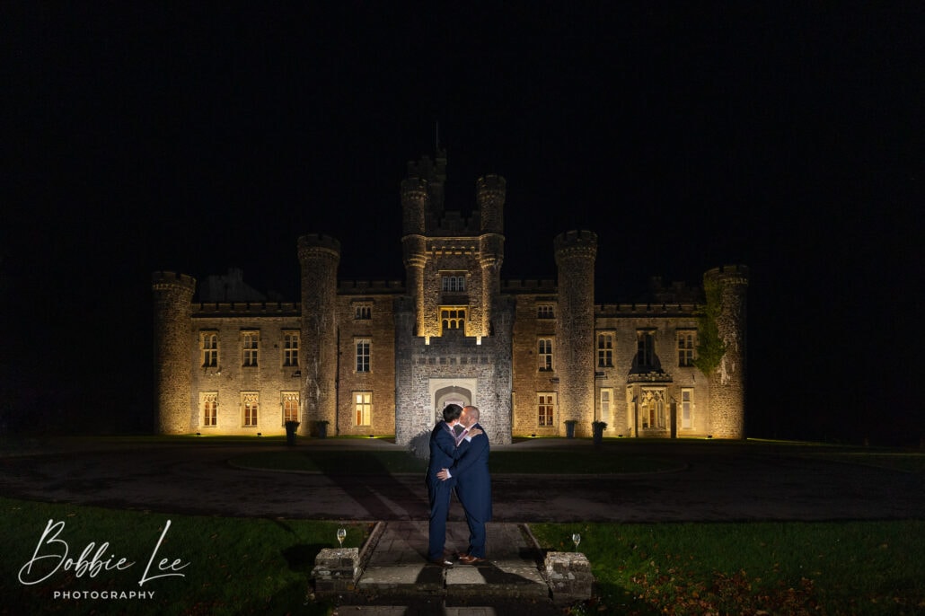 A bride and groom standing in front of a castle at night.