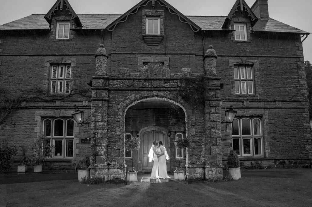 A bride posing elegantly in front of a historic mansion captured by a South Wales wedding photographer.
