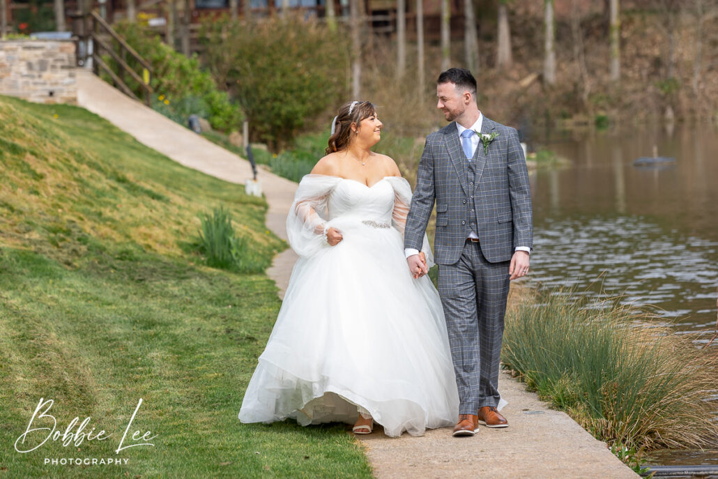 A bride and groom walking along a path near a lake.