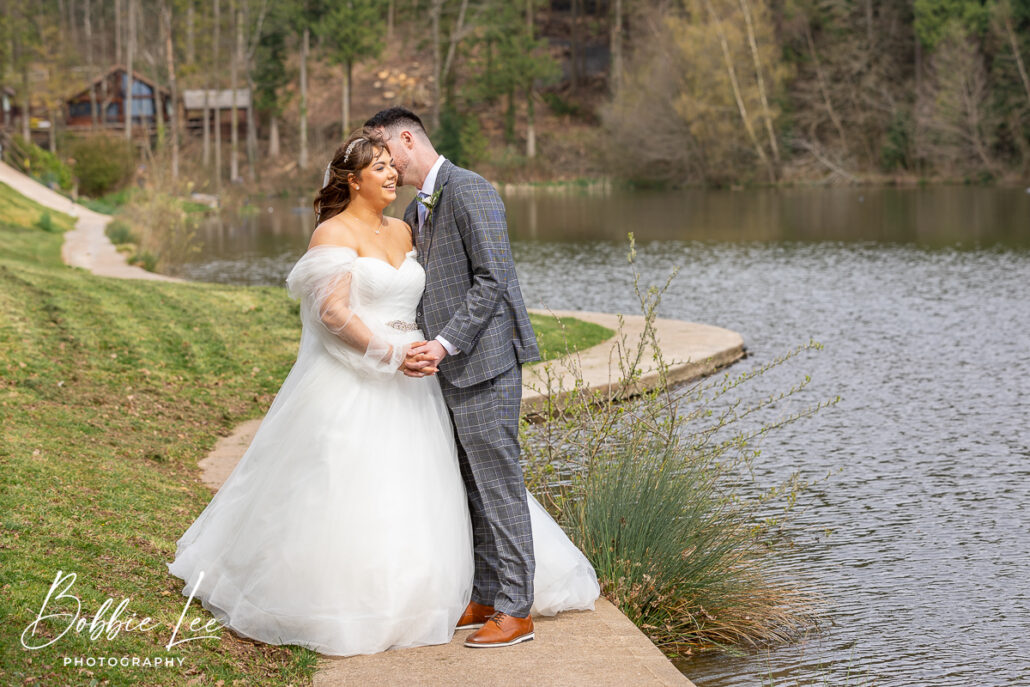 A bride and groom standing next to a pond.