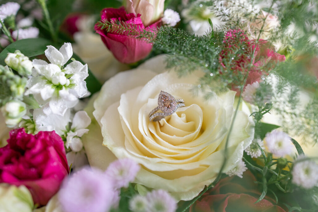 An engagement ring sits on top of a rose.