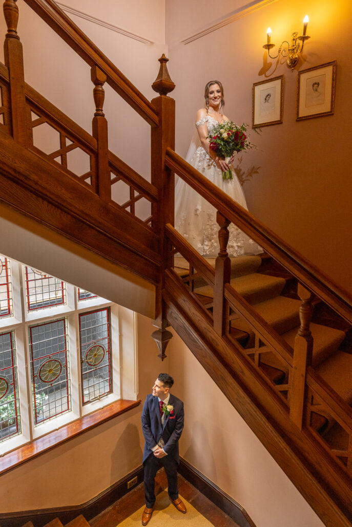 A bride and groom standing on the stairs of a manor house.