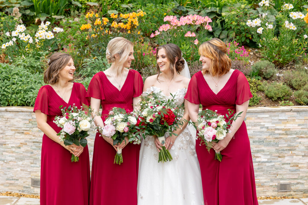 Four bridesmaids in burgundy dresses with bouquets.