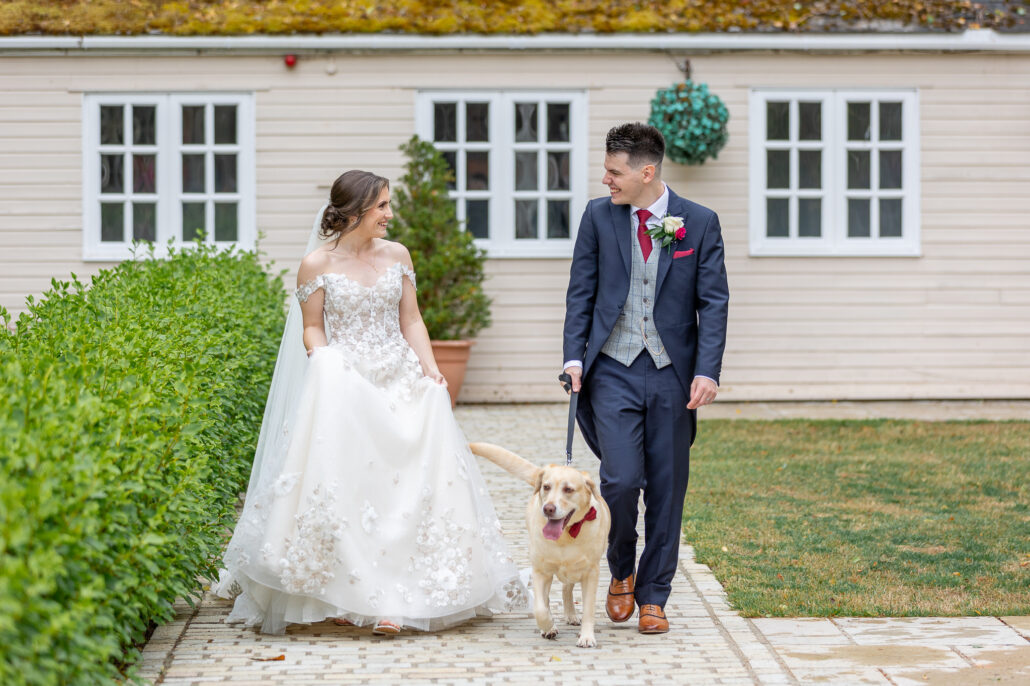 A bride and groom walking their dog in front of a house.