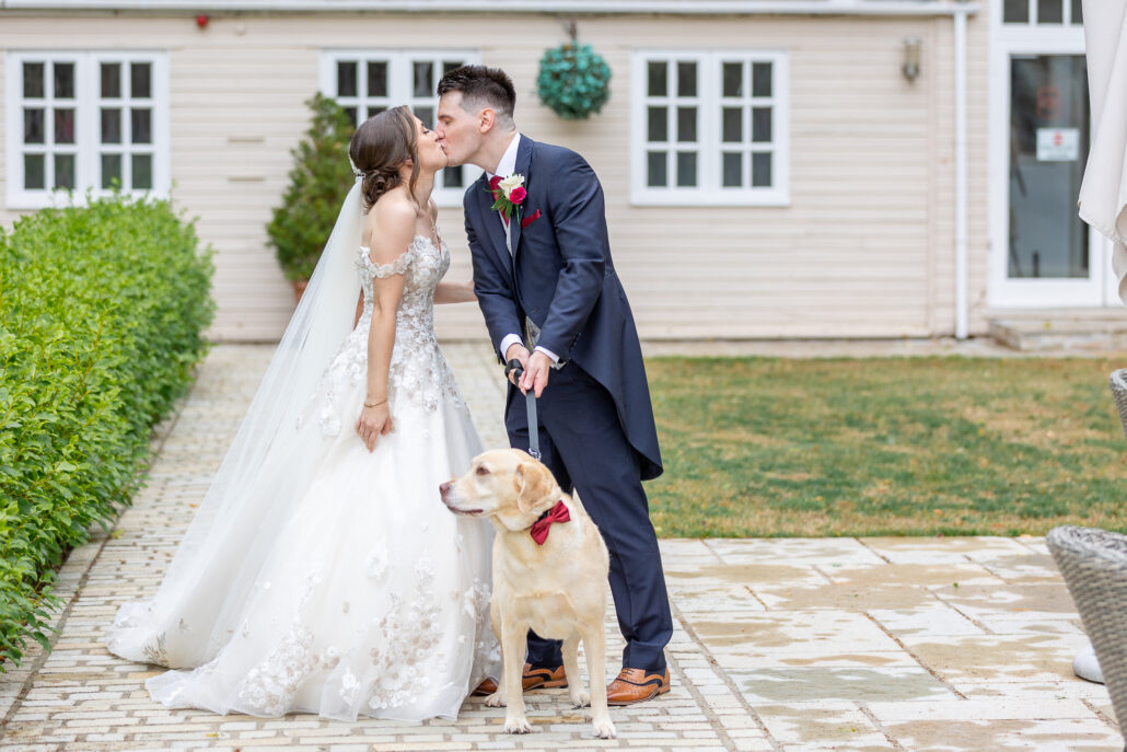 A bride and groom kissing in front of a house with their dog.