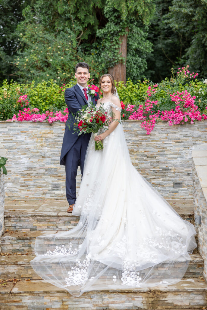 A bride and groom standing on steps in a garden.
