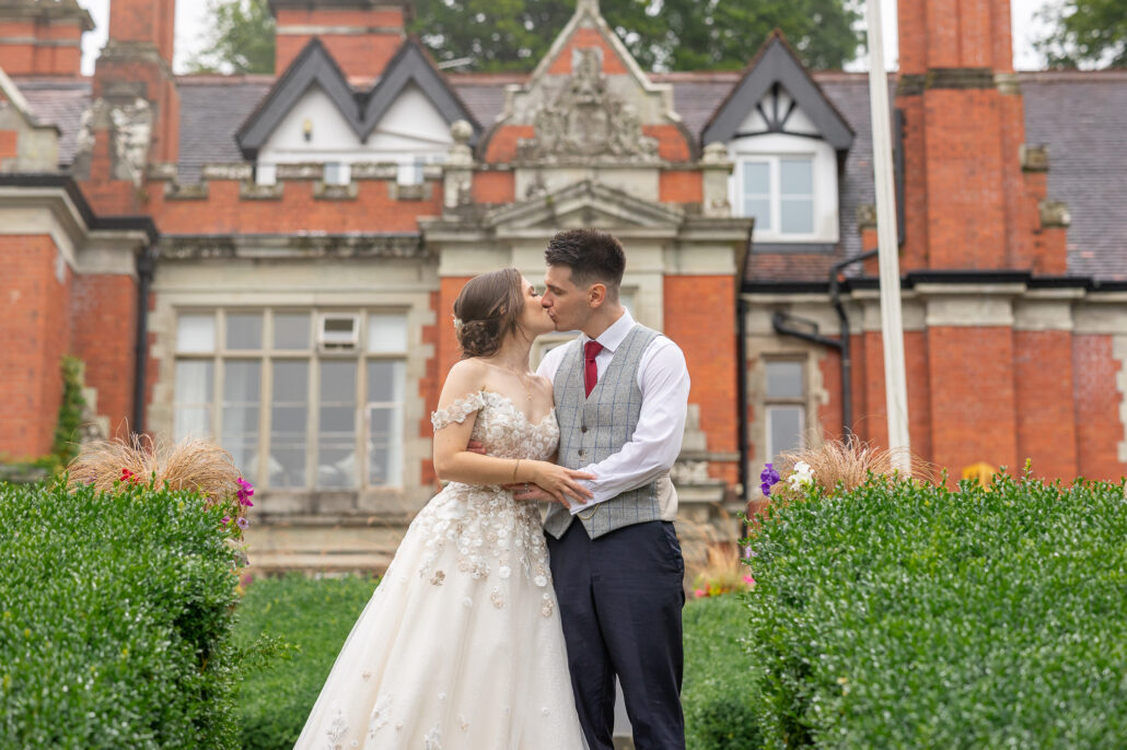 A bride and groom kissing in front of a large mansion.