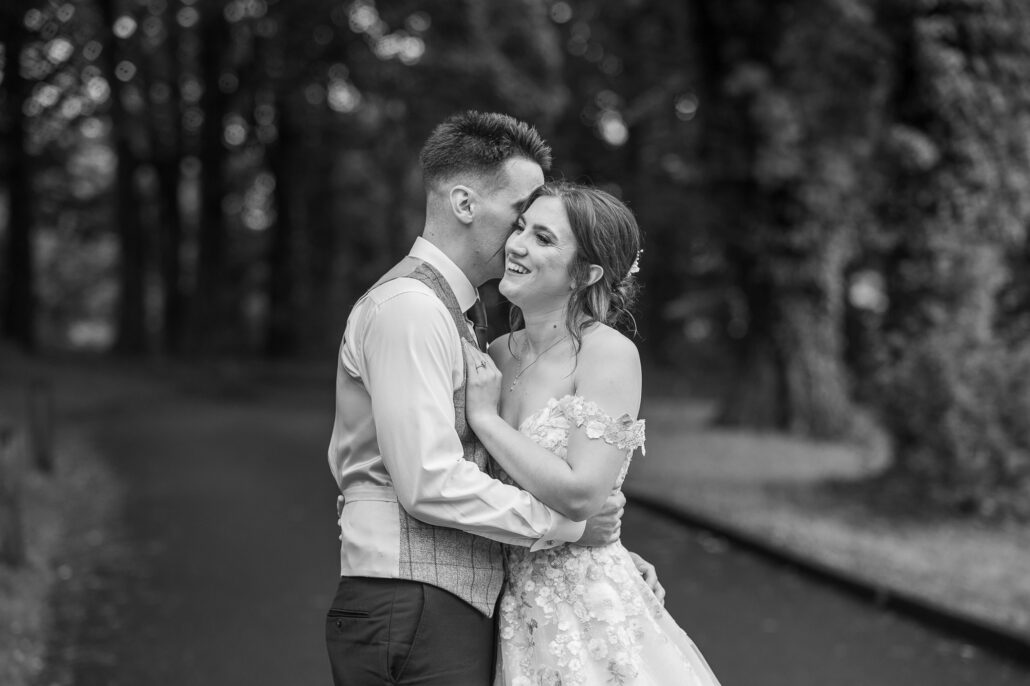 Black and white photo of a bride and groom embracing in the woods.
