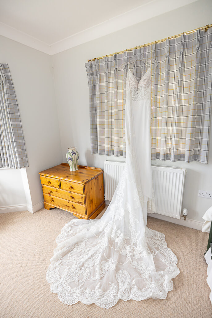 A wedding dress hangs on a dresser in a bedroom.