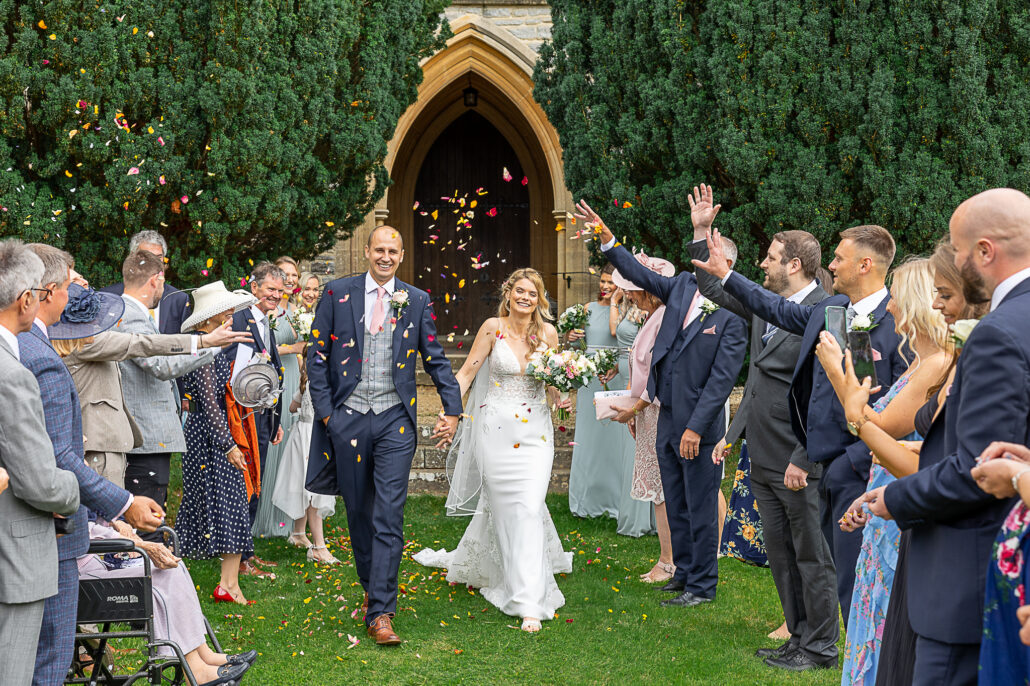 A bride and groom exiting a church with confetti thrown at them.