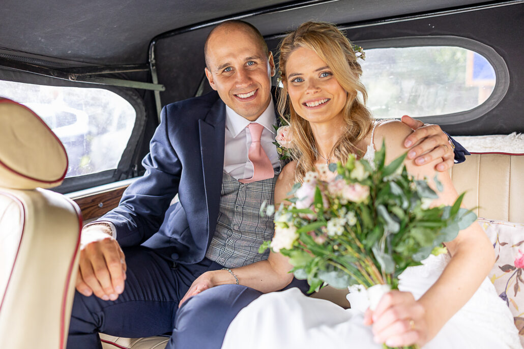 A bride and groom sitting in the back of a vintage car.