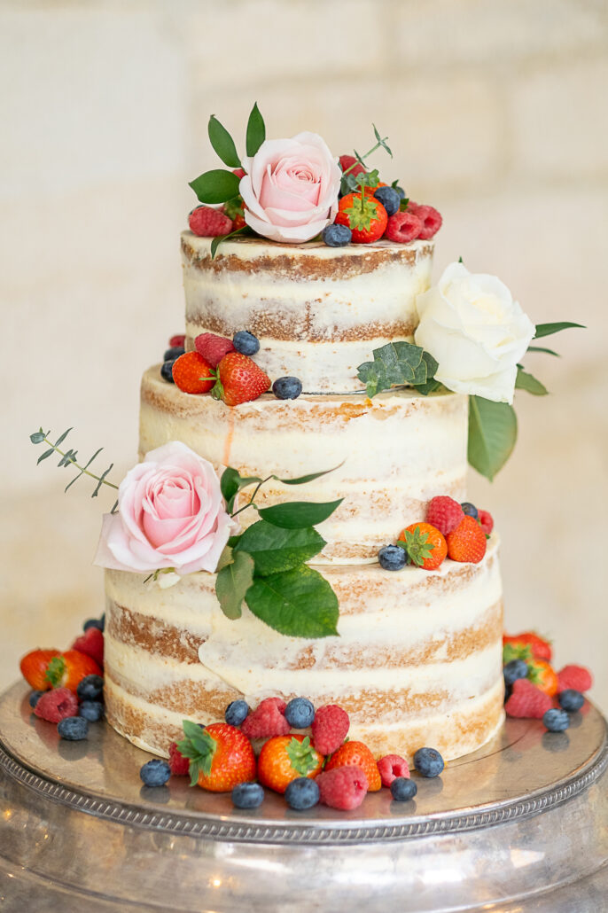 A three tier cake with berries and flowers on top.