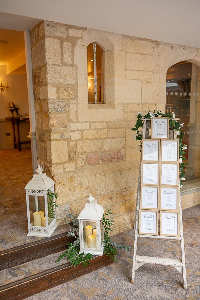 A table with a sign and lanterns in front of a stone wall.