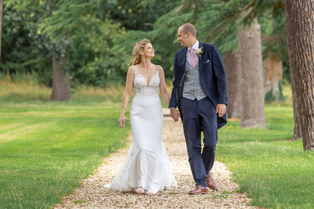 A bride and groom walking down a path in a park.