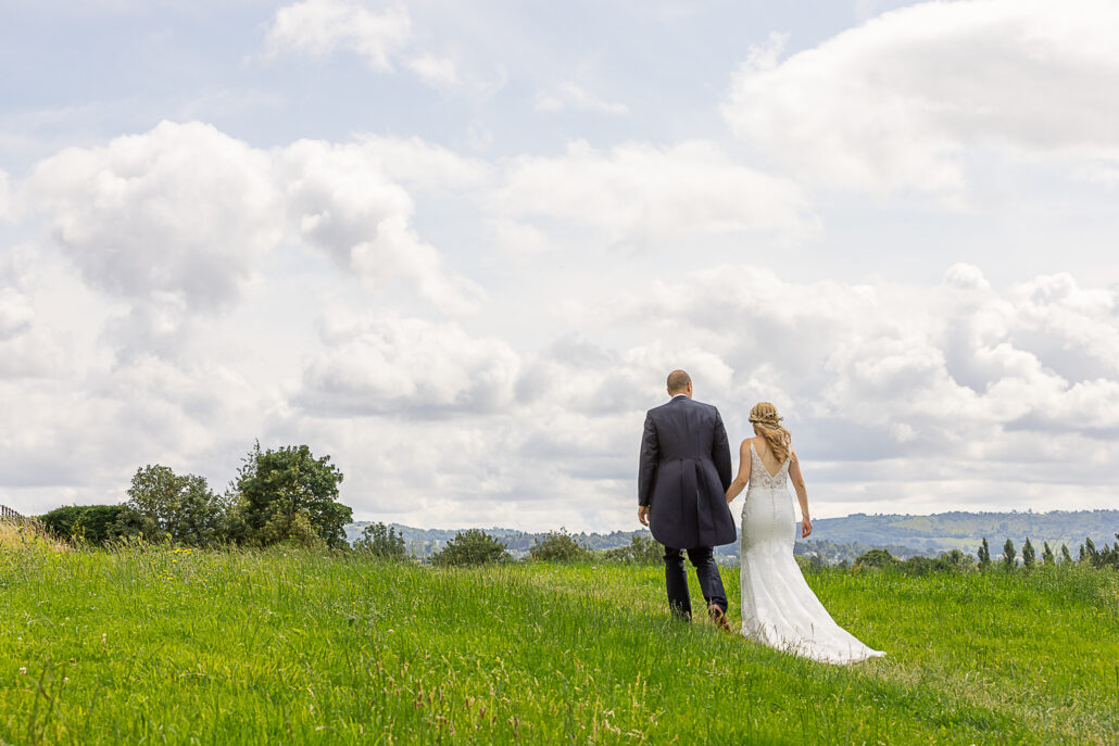 A bride and groom walking through a grassy field.
