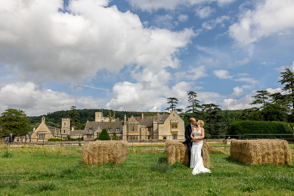 A bride and groom standing in front of hay bales.