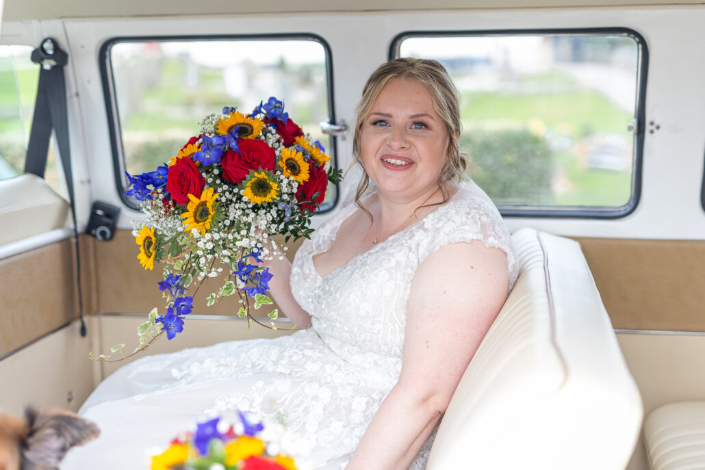 A bride sits in the back seat of a vw camper van.