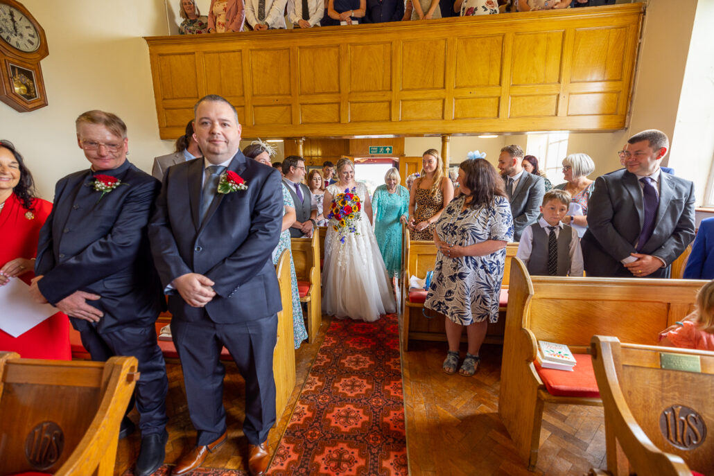 A wedding ceremony in a church with people standing in the pews.