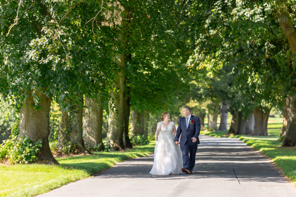 A bride and groom walking down a path lined with trees.