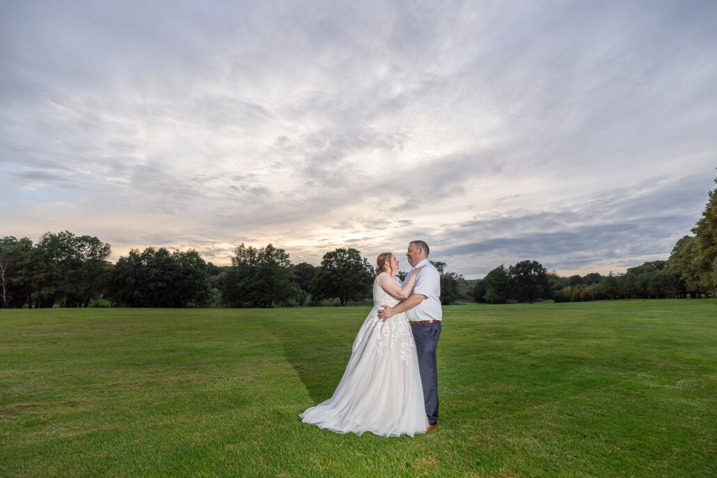 A bride and groom embracing in a field at sunset.