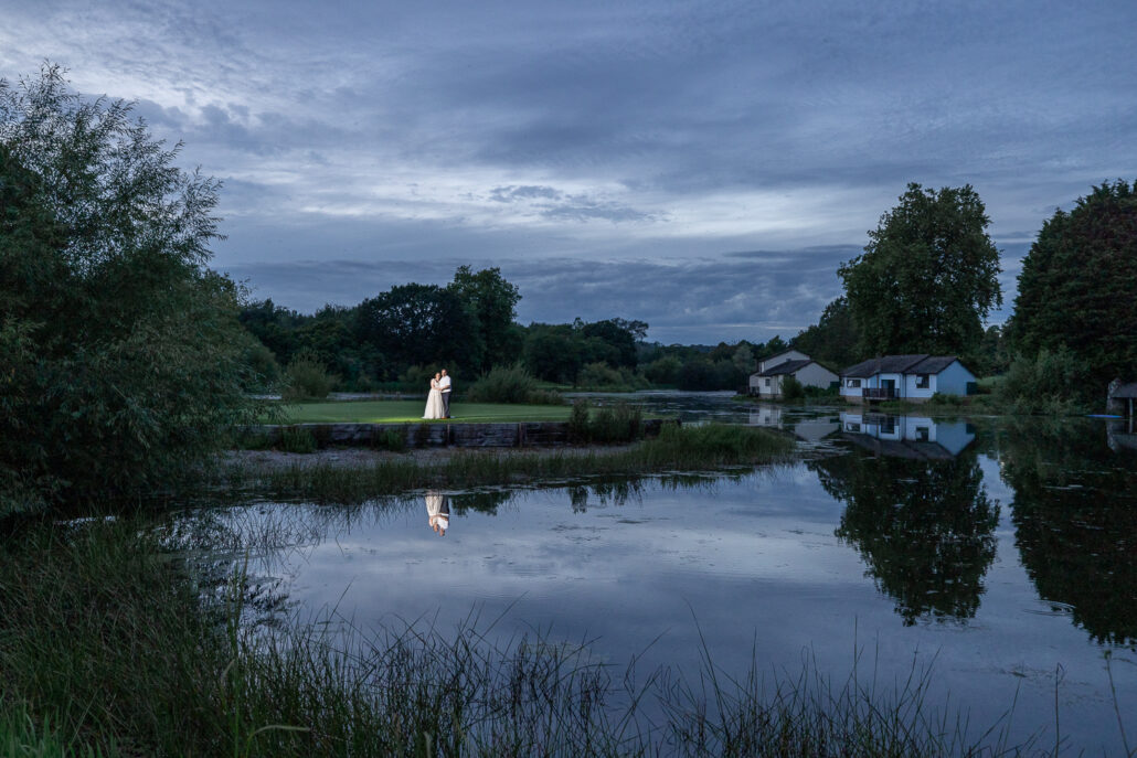 A bride standing in front of a pond at dusk.