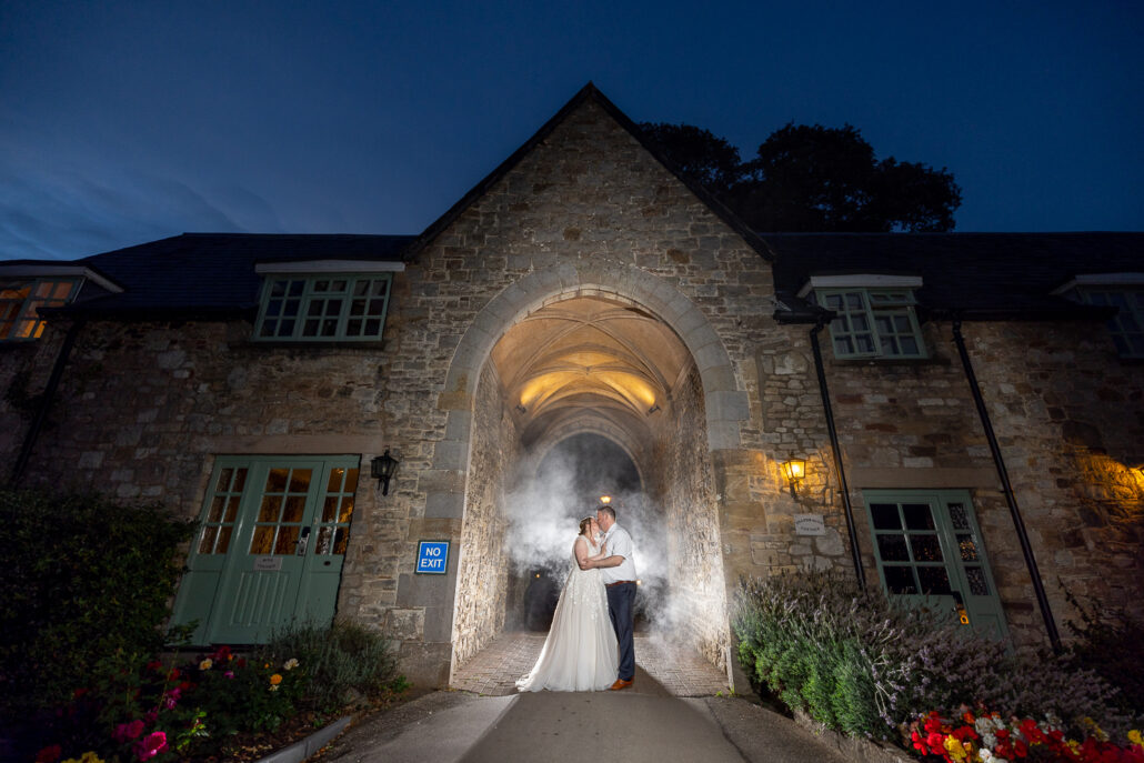 A bride and groom standing in front of a stone archway at night.