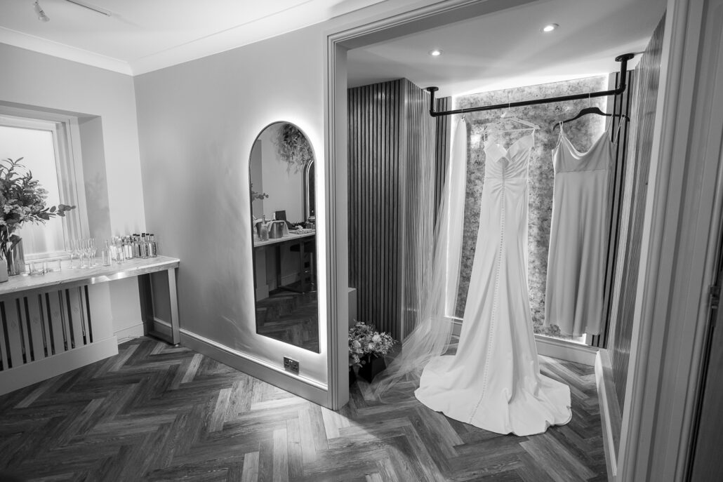A black and white photo of a wedding dress hanging in a closet.