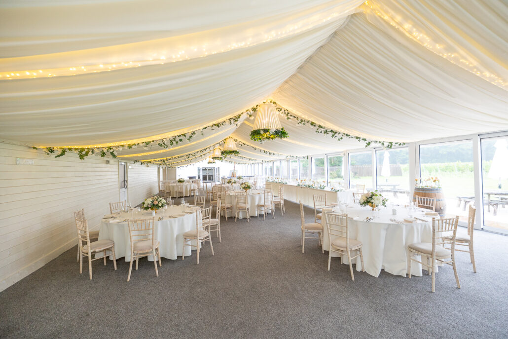 A wedding reception in a white tent with white tables and chairs.