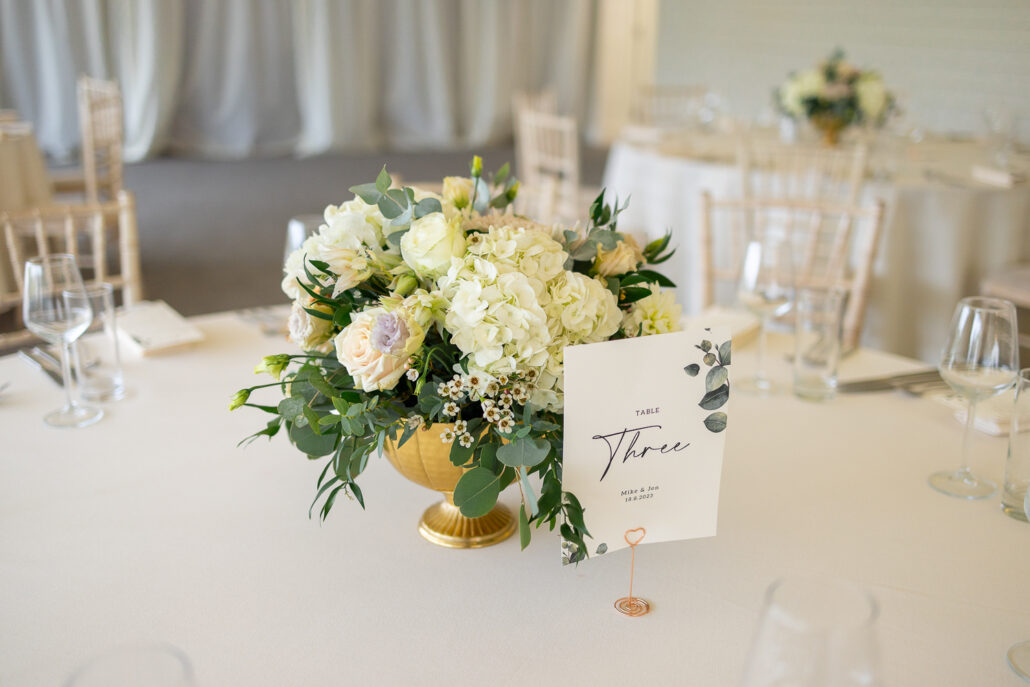 A gold vase with flowers on a table at a wedding reception.