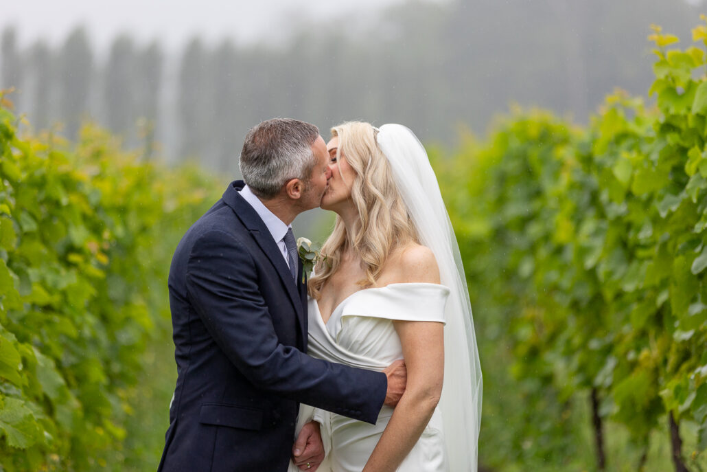 A bride and groom kissing in a vineyard.