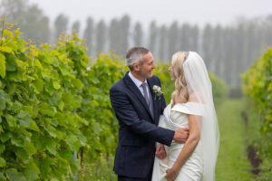 A bride and groom standing in a vineyard on a foggy day.