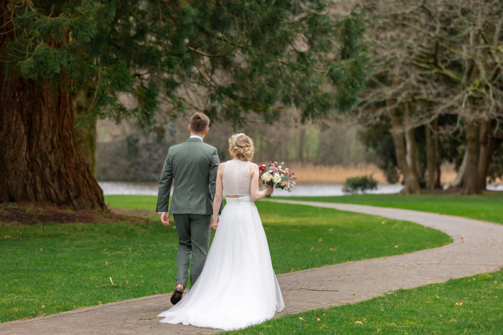 A bride and groom walking down a path near a lake.