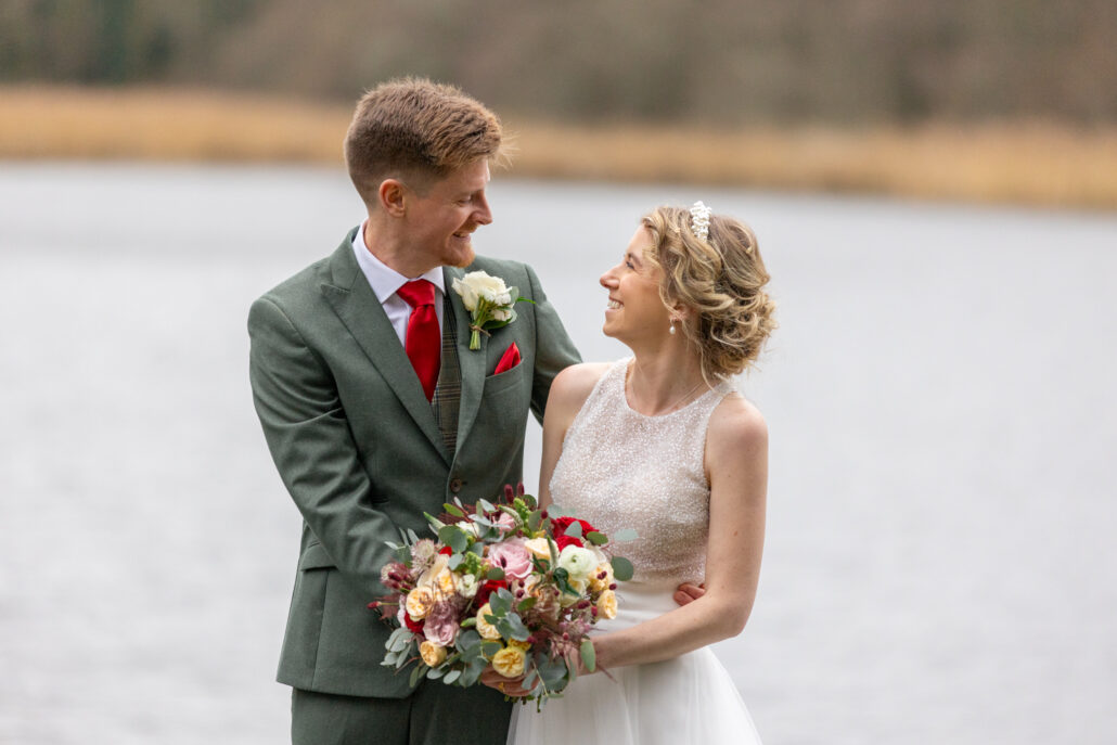 A bride and groom standing in front of a lake.