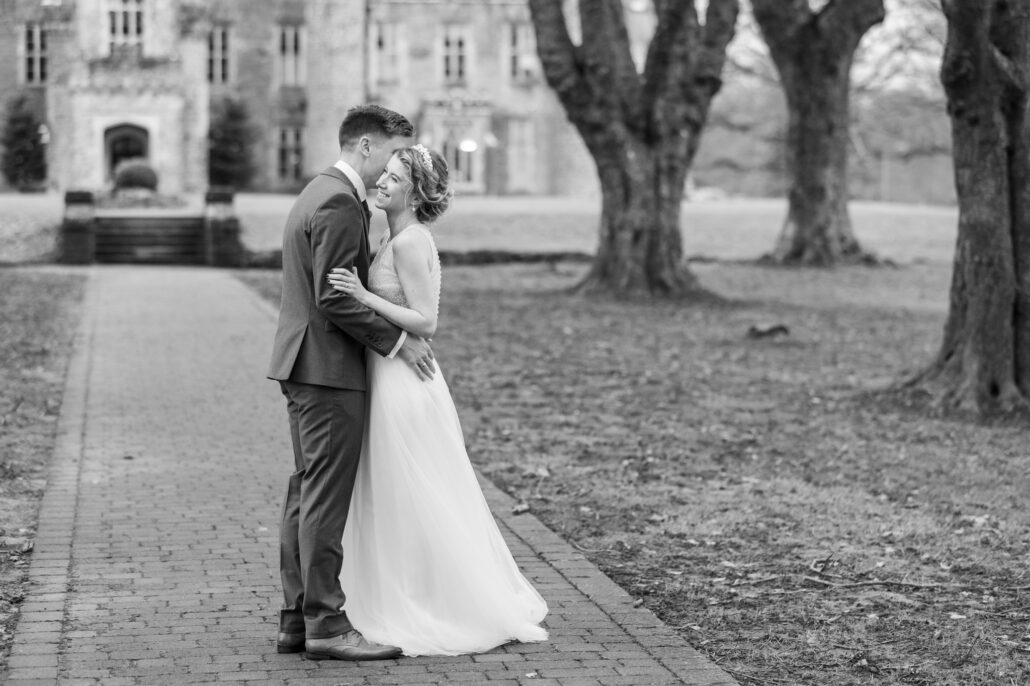 A bride and groom embracing in front of a castle.