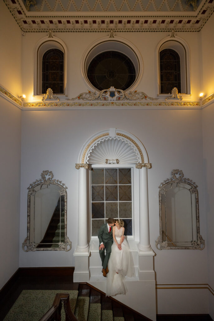 A bride and groom standing on the stairs of an ornate building.
