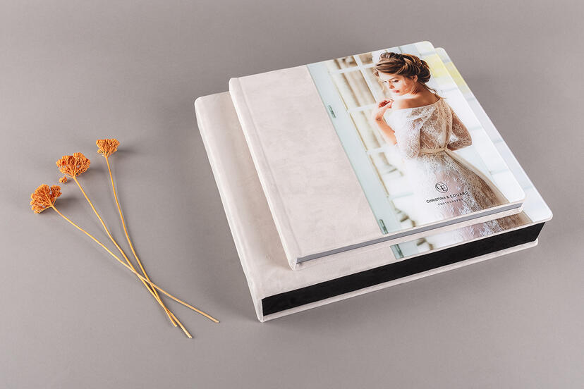 Two photo albums rest on a gray surface next to dried orange flowers. The top album features a cover image of a bride in a lace dress.
