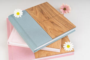 A stack of two books with wooden covers, decorated with white daisies, and a single pink flower in the background.